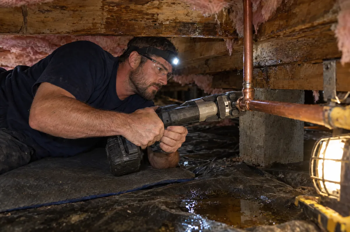 Plumber with a headlamp repairing a copper supply line in a damp crawlspace